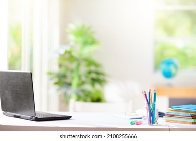 Kids Desk With Laptop And Books. Child Room. Computer For Online Remote Learning In Student Bedroom With White Table And Windows. Homework, Study And Reading Workplace.