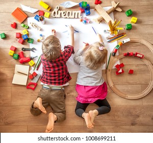Kids drawing on floor on paper. Preschool boy and girl play on floor with educational toys - blocks, train, railroad, plane. Toys for preschool and kindergarten. Children at  home or daycare. Top view - Shutterstock ID 1008699211