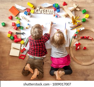 Kids drawing on floor on paper. Preschool boy and girl play on floor with educational toys - blocks, train, railroad, plane. Toys for preschool and kindergarten. Children at  home or daycare. Top view - Shutterstock ID 1009017007