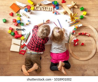 Kids drawing on floor on paper. Preschool boy and girl play on floor with educational toys - blocks, train, railroad, plane. Toys for preschool and kindergarten. Children at  home or daycare. Top view - Shutterstock ID 1018901002