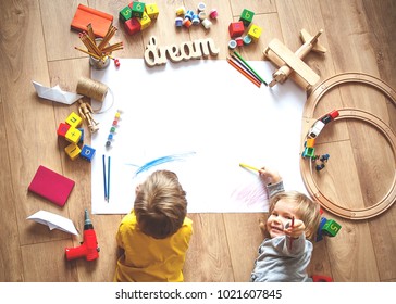 Kids drawing on floor on paper. Preschool boy and girl play on floor with educational toys - blocks, train, railroad, plane. Toys for preschool and kindergarten. Children at  home or daycare. Top view