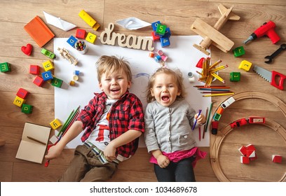 Kids drawing on floor on paper. Preschool boy and girl play on floor with educational toys - blocks, train, railroad, plane. Toys for preschool and kindergarten. Children at home or daycare. Top view - Shutterstock ID 1034689678