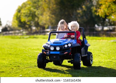 Kids driving electric toy car in summer park. Outdoor toys. Children in battery power vehicle. Little boy and girl riding toy truck in the garden. Family playing in the backyard.
