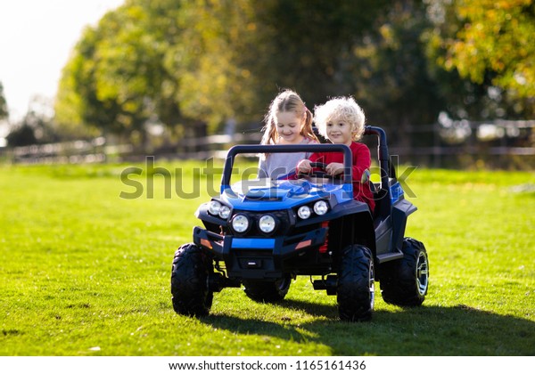 Kids driving\
electric toy car in summer park. Outdoor toys. Children in battery\
power vehicle. Little boy and girl riding toy truck in the garden.\
Family playing in the\
backyard.