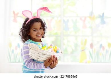 Kids dyeing Easter eggs. Children in bunny ears dye colorful egg for Easter hunt. Home decoration with flowers, basket and rabbit for spring holiday celebration. Little curly boy decorating home. - Powered by Shutterstock