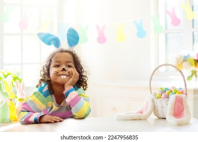 Kids dyeing Easter eggs. Children in bunny ears dye colorful egg for Easter hunt. Home decoration with flowers, basket and rabbit for spring holiday celebration. Little curly boy decorating home.