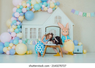 Kids Dyeing Easter Eggs. Girl In Bunny Ears Dye Colorful Egg For Easter Hunt. Home Decoration With Flowers, Basket And Rabbit For Spring Holiday Celebration.