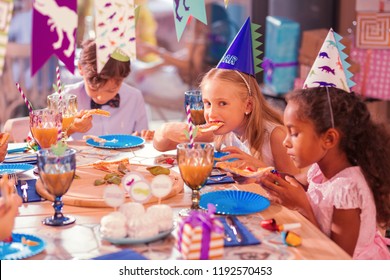 Kids eating pizza. Calm thoughtful children attending birthday party and eating pizza at the big table - Powered by Shutterstock