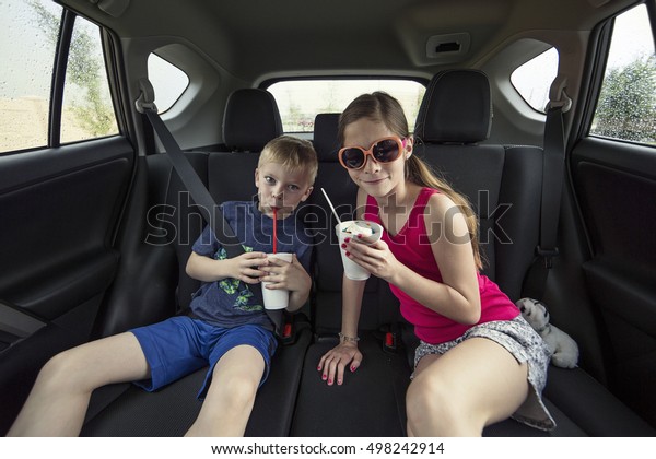 Kids eating a treat in the back of their car\
after going to a drive thru\
restaurant