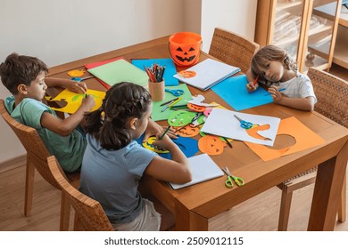 Kids Engaged In A Halloween Craft Activity, Creating Paper Pumpkins And Other Decorations At A Table With Various Supplies.Children Making Halloween Crafts At Home - Powered by Shutterstock