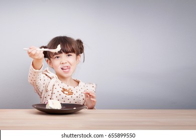 Kids Enjoy Eating Concept : Happy Little Cute Mixed Race Girl Enjoy Eating Cake With Smiley Face , Tongue Stick With Spoon In Her Hand For Invite To Eat. Kid Poster Background.