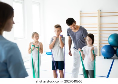 Kids exercising with tapes, helpful trainer standing behind them