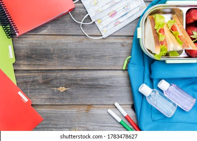 Kid's Face Mask, Lunchbox With Sandwiches, Strawberries, Bottles Of Sanitizer.Blue Backpack With Notebooks,pens,box On Wooden Background.Back To School.Lunch With Safety Precautions After Coronavirus.