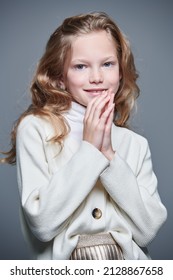 Kid's fashion. Portrait of a cute joyful 11 year old girl with blonde hair and freckles posing at studio in fashionable classical kid's clothes. Gray background.