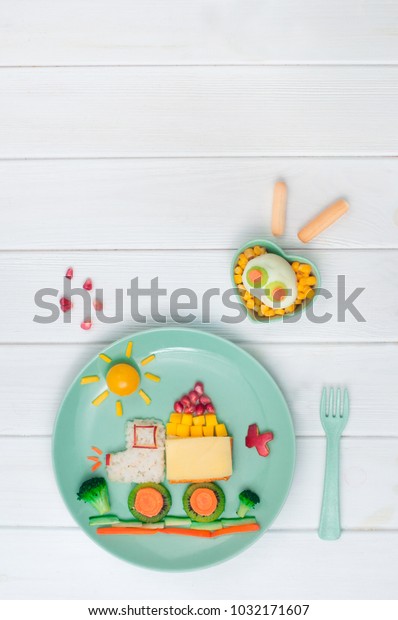 Kids food art: Car from rice, sandwich\
and fresh fruits and vegetables on the plate on white wooden\
background with blank space for text; top view, flat\
lay