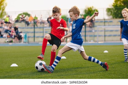 Kids Football Players Kicking Ball on Soccer Field. Sports Soccer Horizontal Background. Spectators on Stadium in the Background. Youth Junior Athletes in Red and Blue Soccer Shirts. Sports Education