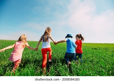 Kids Friends Run Across A Green Field. View From The Back