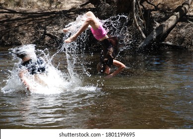 Kids Frolicking In The River.  Girl Lifted Up To Do A Backflip Into The Water.  Water Droplets, Her In Mid-air.  Lots Of Carefree Fun.