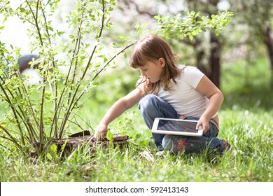 Kids girl playing with a tablet on a stump, spring, childhood outdoors, explores the nature - Powered by Shutterstock