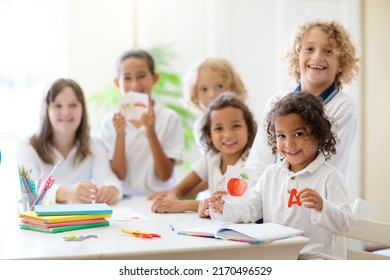 Kids Go Back To School. Interracial Group Of Children Of Mixed Age In Classroom. Students Learn To Read And Write. Preschooler Or Kindergarten Kid With Teacher. Child Learning Letters With Flash Cards