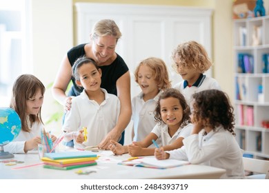 Kids go back to school. Interracial group of children of mixed age in classroom. Students learn to read and write. Preschooler or kindergarten kid with teacher. Child learning letters with flash cards - Powered by Shutterstock