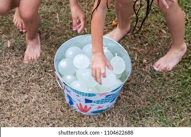 Kids Grabbing Water Balloons From A Colorful Metal Bucket On A Hot Summer Day For A Water Fight In The Garden.