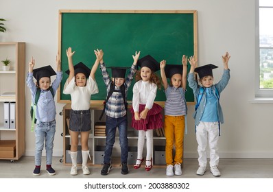 Kids graduate. Portrait of funny little kindergarten or junior high school graduates who are dressed in mortar boards. Kids having fun in the classroom on the background of the school board.