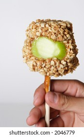 Kids Hand Holding A Carmel Apple With Nuts And A Bite Taken Out Of It.