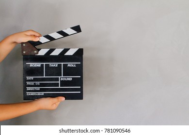 Kid's hand holding film clapper board with gray concrete loft style wall background texture. Concept for movie and video production, film director.