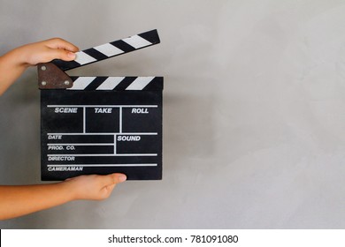 Kid's hand holding film clapper board with gray concrete loft style wall background texture. Concept for movie and video production, film director.