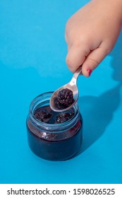 Kids Hand Holding Spoon With Berries. Jar Of Blackberry Jam On Blue Paper. Selective Focus.