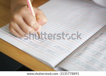 The kid's hand is practicing writing English cursive handwriting sentences in a notebook with a pencil. Cursive handwriting practice.  Kindergarten writing skills. Self-learning education. Copy space.