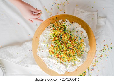 Kid's hand sprinkling sprinkles on a vanilla cream cake for her mom's birthday