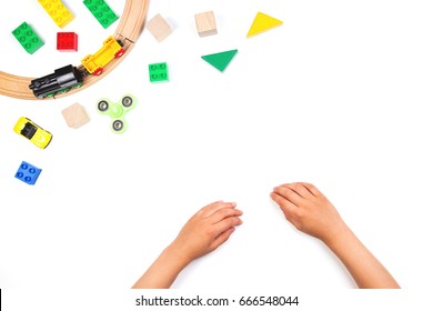 Kid's Hands And Colorful Toys. Fidget Spinner, Cars, Toy Train, Rails, Bricks And Blocks On White Background