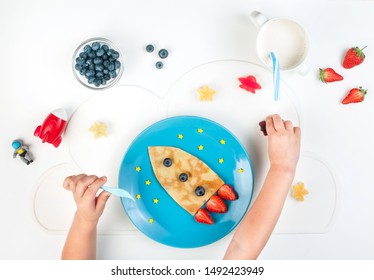 Kids Hands Eating Pancake Served As A Rocket On The Blue Plate On White Table. Top View, Flat Lay. 