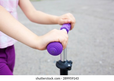 Kids Hands Holding Handlebar On Scooter Or Bicycle In An Urban Neighborhood