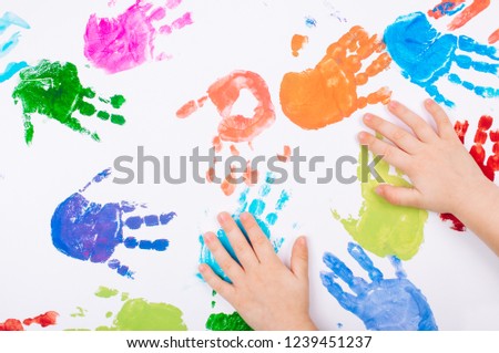 Kid's hands making colored handprints on white background. Top view, flat lay.