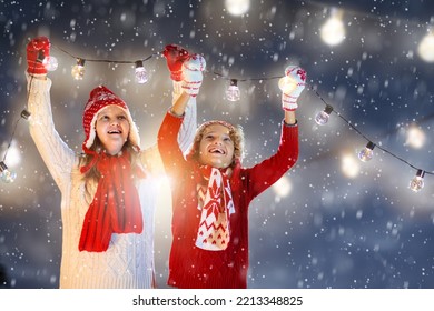 Kids hanging Christmas lights. Family decorating home with fairy light in snow. Parents and children decorate house on snowy cold evening. Xmas celebration. Winter holiday fun. Child holding lamp. - Powered by Shutterstock