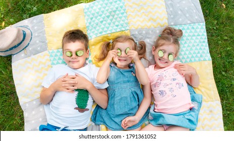 Kids Have Fun At Summer Camp During The Holidays. Ideas For Fun Activities In The Summer. Children Play On A Patchwork Rug. Kids Put Pieces Of Cucumber Over Their Eyes