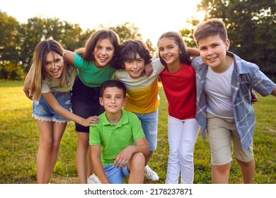 Kids Having Fun Outdoors In Summer. Group Portrait Of Happy Little School Children In The Park. Bunch Of Cheerful Friends Posing For A Group Photo, Hugging, Looking At The Camera And Smiling