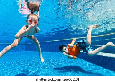 Kids Having Fun Playing Underwater In Swimming Pool On Summer Vacation