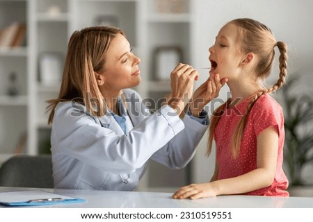Kids Healthcare. Female doctor pediatrician checking throat of little girl patient, cute female child having checkup in modern clinic, suffering angina or tonsillitis, having strep, closeup