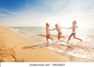 Kids holding hands and running along sandy beach - Powered by Shutterstock