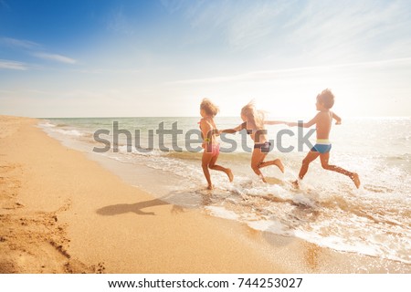 Kids holding hands and running along sandy beach