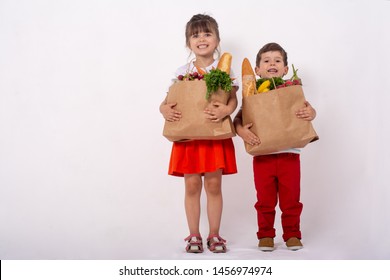 Kids Holding Paper Grocery Bag Full Of Vegetables Milk, Bread. Happy Family With Grocery Bag Full Of Healthy Food Isolated On White. Food In Paper Bag. Grocery Shopping Concept.