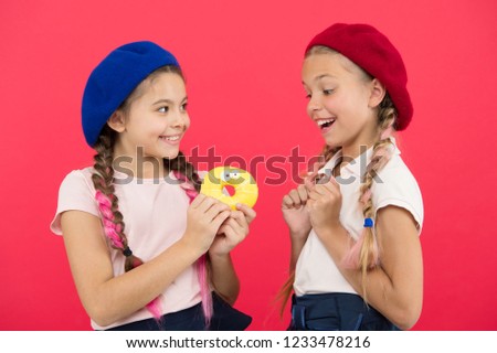 Kids huge fans of baked donuts. Share sweet donut. Girls in beret hats hold glazed donut red background. Kids playful girls ready eat donut. Friendship and generosity. Sweets shop and bakery concept.