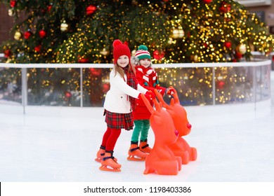 Kids Ice Skating In Winter Park Rink. Children Ice Skate On Christmas Fair. Little Girl And Boy With Skates On Cold Day. Snow Outdoor Fun For Child. Winter Sports. Xmas Family Vacation With Kid.