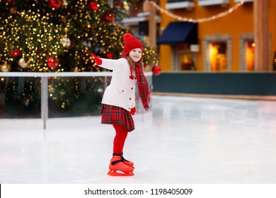 Kids Ice Skating In Winter Park Rink. Children Ice Skate On Christmas Fair. Little Girl With Skates On Cold Day. Snow Outdoor Fun For Child. Winter Sports. Xmas Family Vacation With Kid.