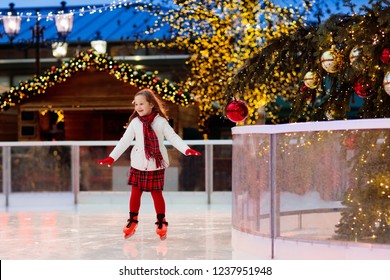 Kids Ice Skating In Winter Park Rink. Children Ice Skate On Christmas Fair. Little Girl With Skates On Cold Day. Snow Outdoor Fun For Child. Winter Sports. Xmas Family Vacation With Kid.