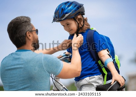 Kids insurance. Father and son concept. Father teaching son riding bike. Father helping his son to wear a cycling helmet. Child in safety helmet.Child in safety helmet learning to ride cycle with dad.